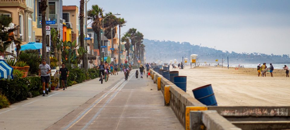 Group of people running and cycling on a wooden San Diego beach boardwalk