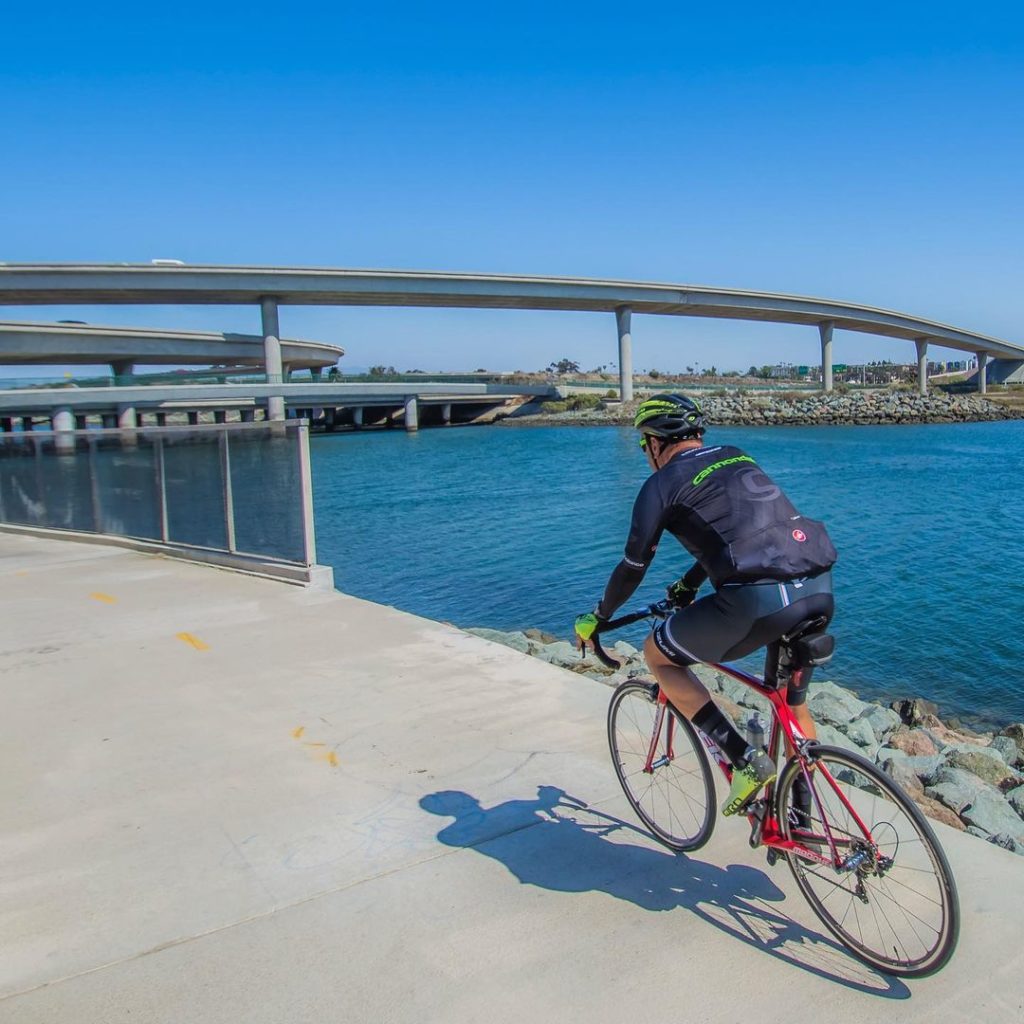 Biker along coastline underneath bridge