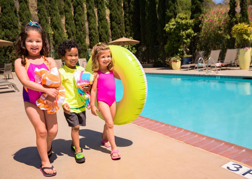 kids walking with towels and floaty next to pool