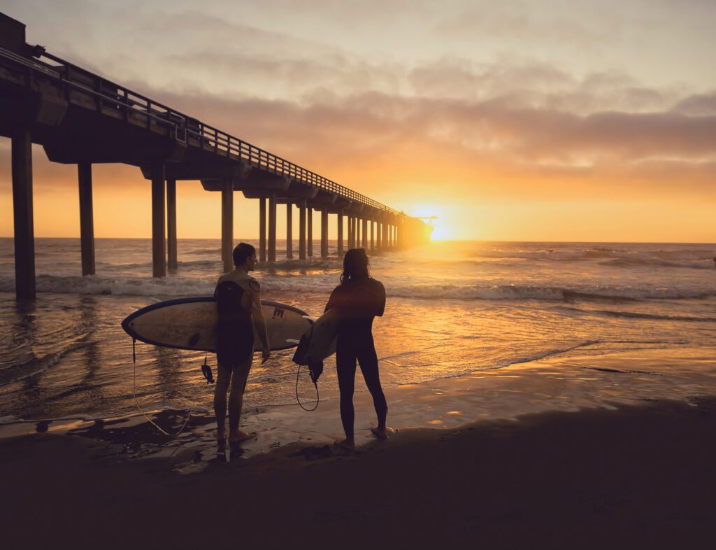 people on the beach with surfboards at sunset