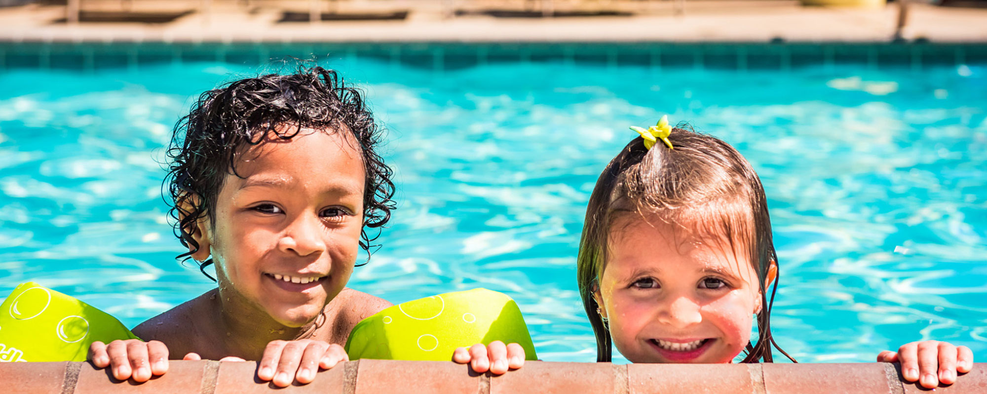 two kids peeking over the edge of the swimming pool