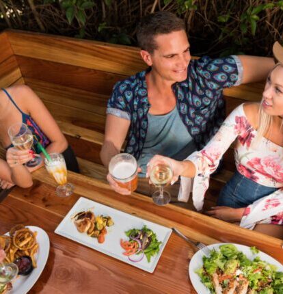 Group of friends enjoying drinks and food at an outdoor restaurant booth.
