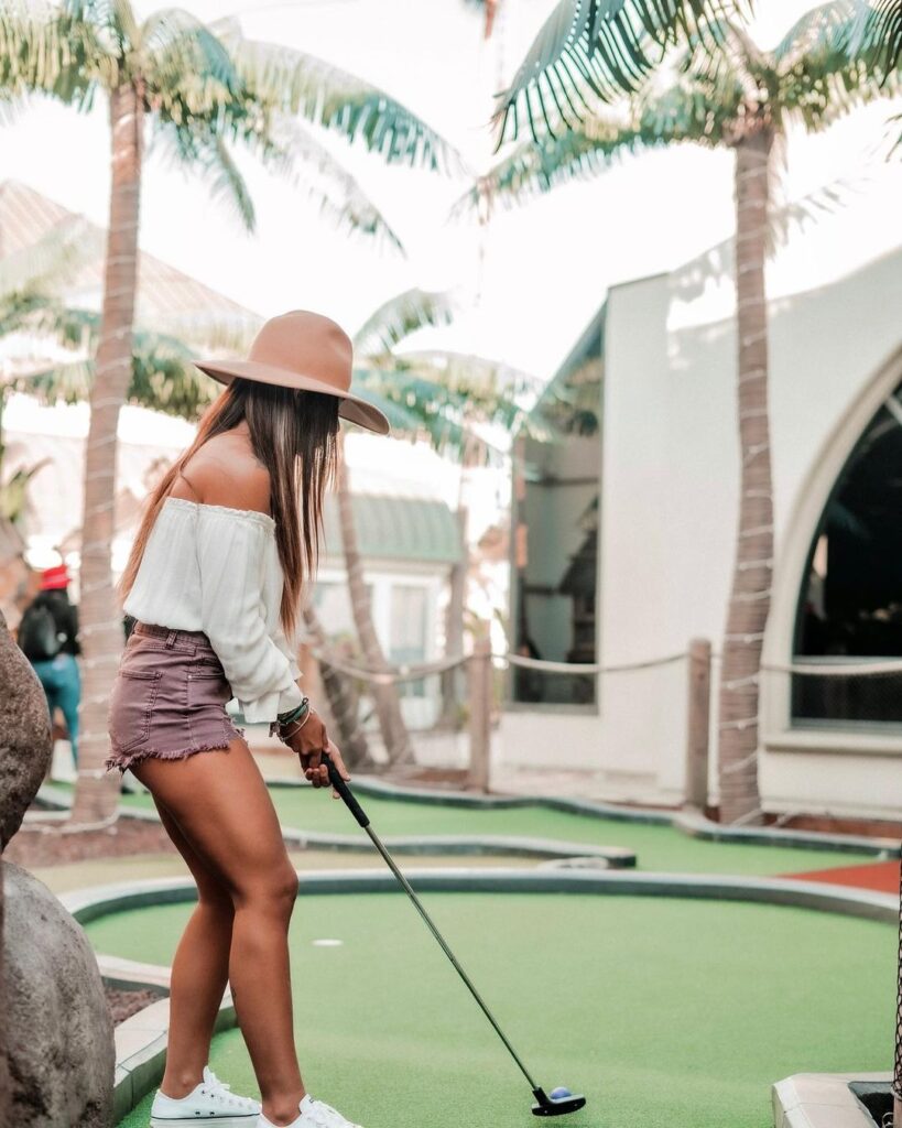 a woman in a sun hat playing miniature golf
