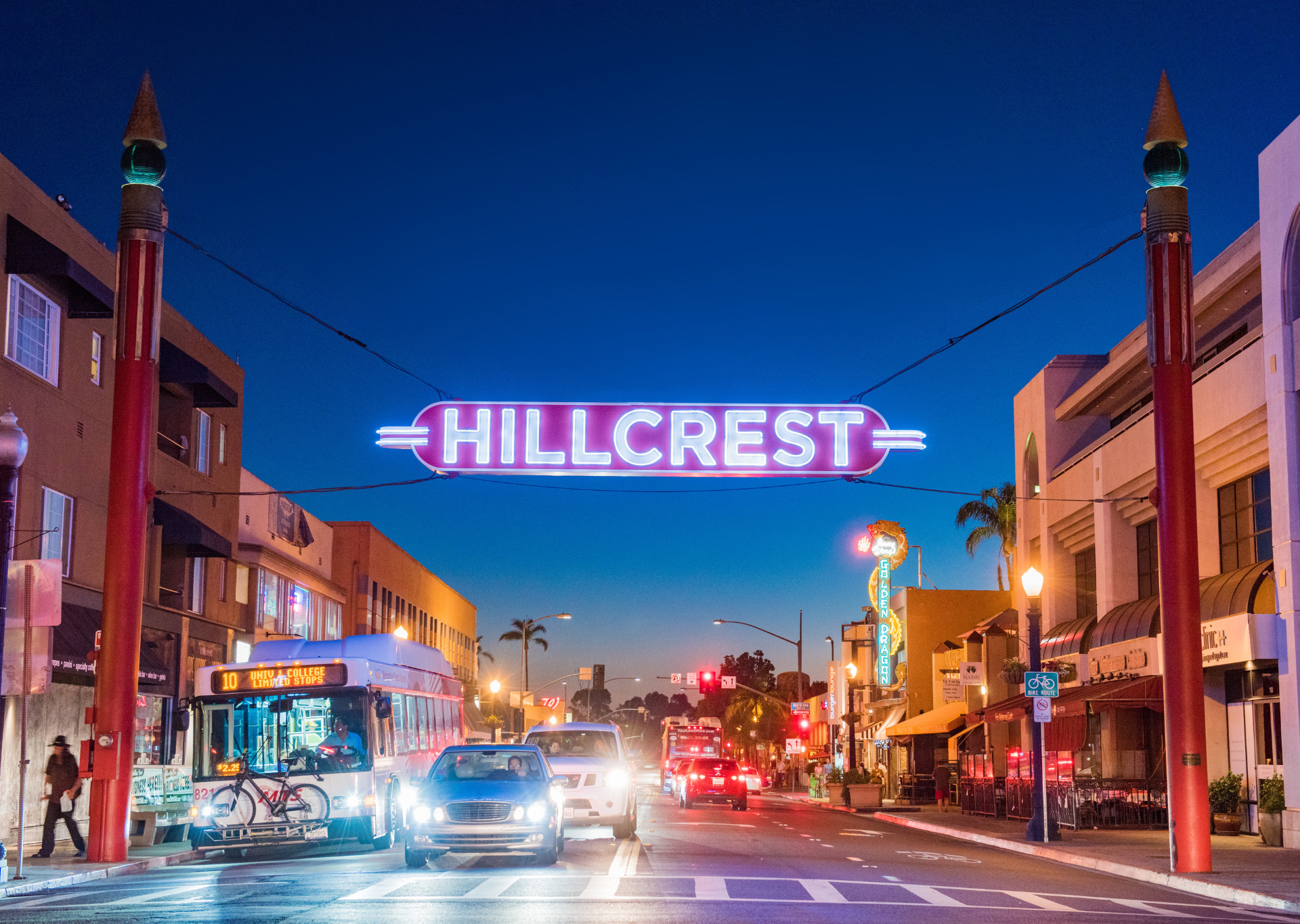 a Hillcrest sign, lit up over a busy street at dusk
