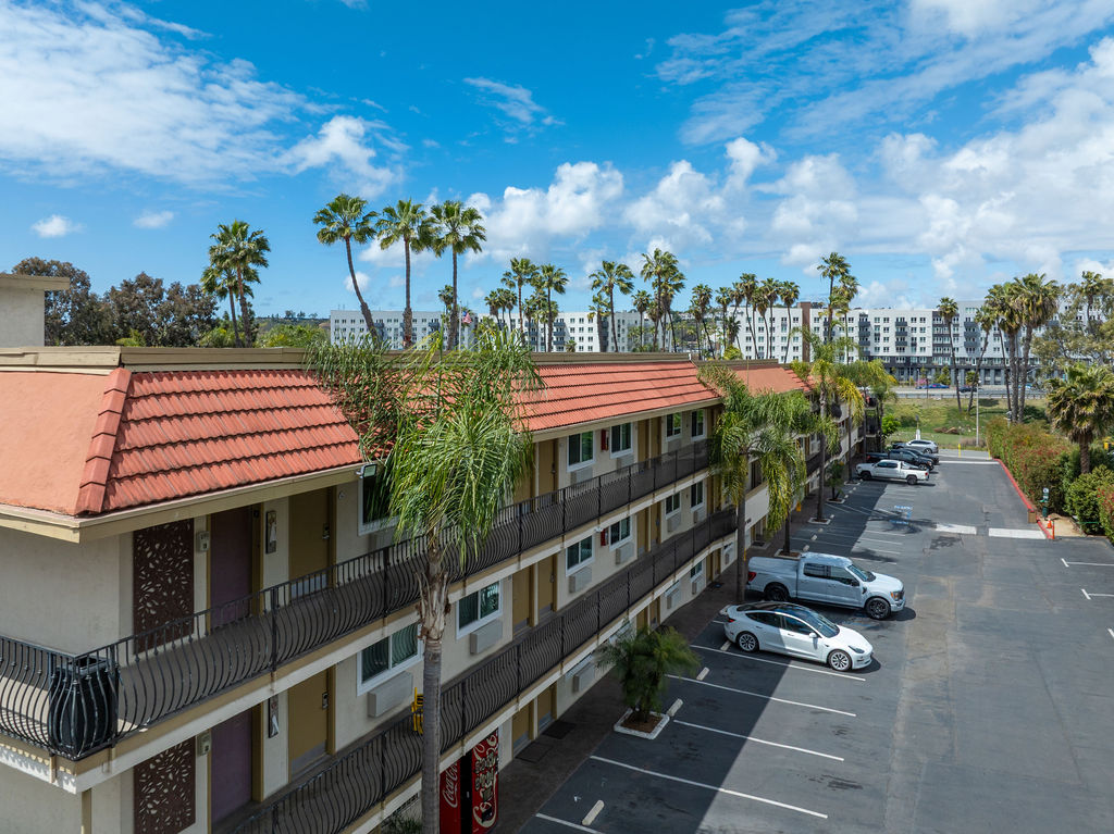 Motel exterior with balconies, palm trees, and parking lot.