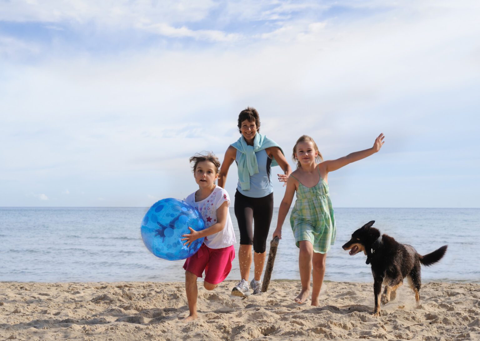 Family with children and dog playing on beach.
